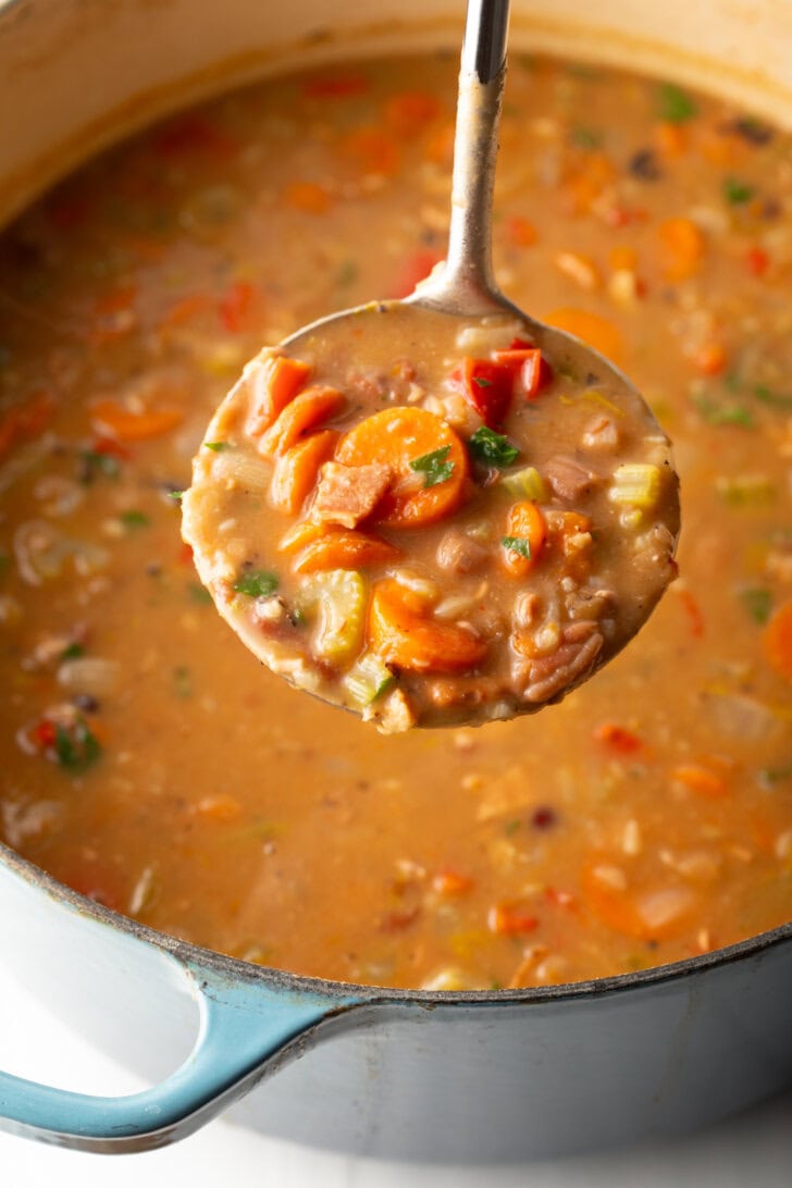 Top down view soup made with 15 beans and veggies in a large cooking pot. A metal ladle is showing a spoonful to camera.