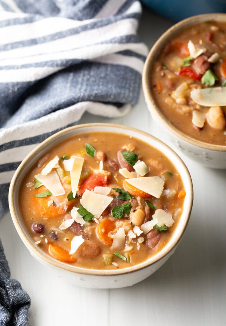 Two white bowls of 15 bean soup, garnished with shaved parmesan.