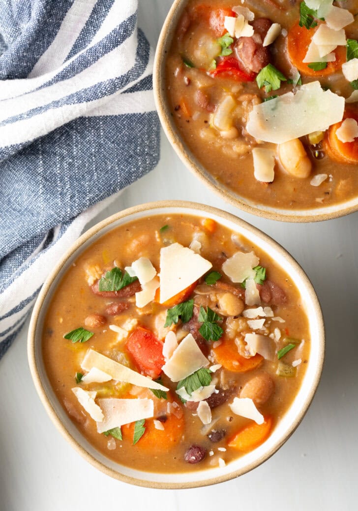 Two white bowls of 15 bean soup, garnished with shaved parmesan.