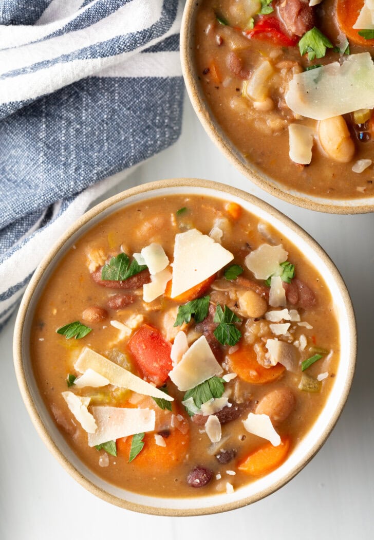 Two white bowls of 15 bean soup, garnished with shaved parmesan.