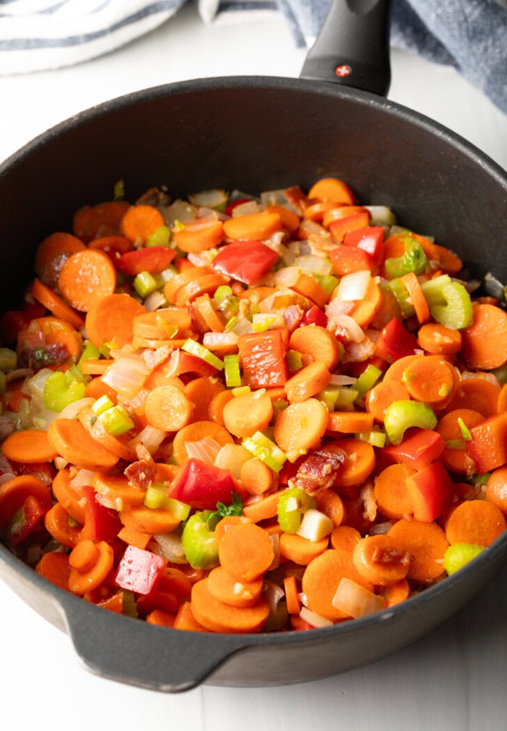 Sliced carrots, onion, garlic, and red pepper sauteeing in a cast iron skillet.