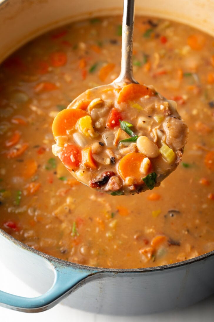 Top down view soup made with 15 beans and veggies in a large cooking pot. A metal ladle is showing a spoonful to camera.