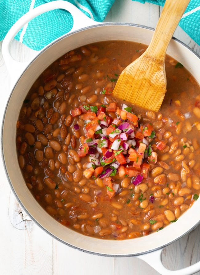 Frijoles de la Olla in a large pot with pico de gallo on top. 