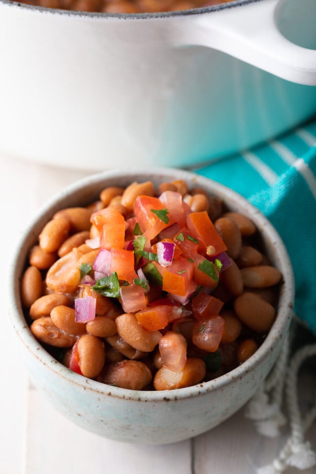 Pinto beans served in a small bowl with pico de gallo on top. 