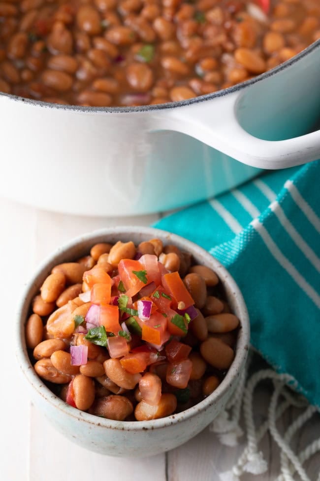 Serving of pinto beans with the pot in the background. Mexican Pinto Beans Recipe (Frijoles de la Olla)