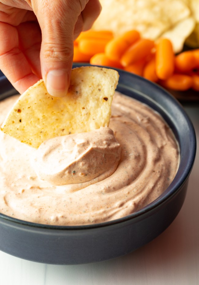 hand with tortilla chip scooping homemade taco dip