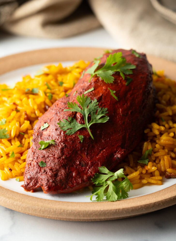 A plate of yellow rice and pollo pibil chicken breast.