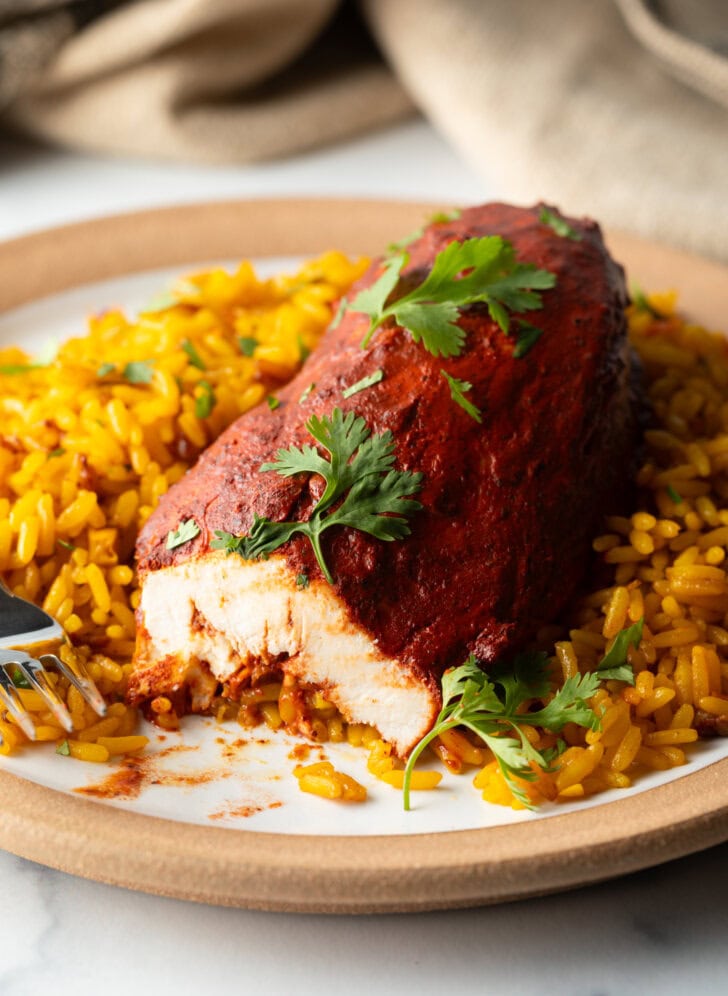 Plate of yellow rice and achiote chicken breast. A fork has take a bite from the chicken to show the inner meat