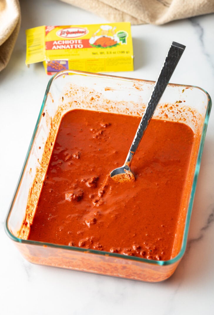 Spoon mixing red marinade in a glass square dish.