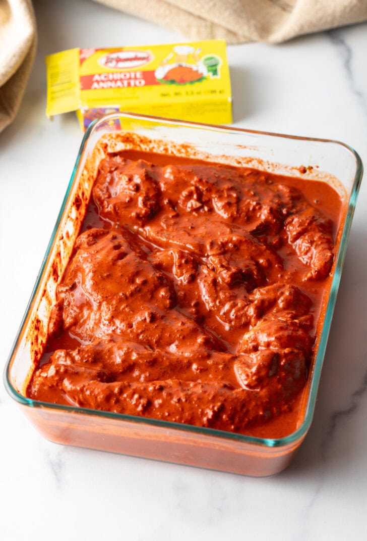 Square glass dish with pieces of raw chicken marinating.