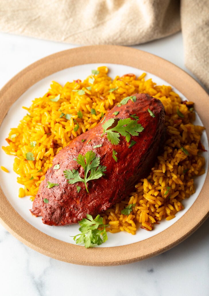 A plate of yellow rice and pollo pibil chicken breast.