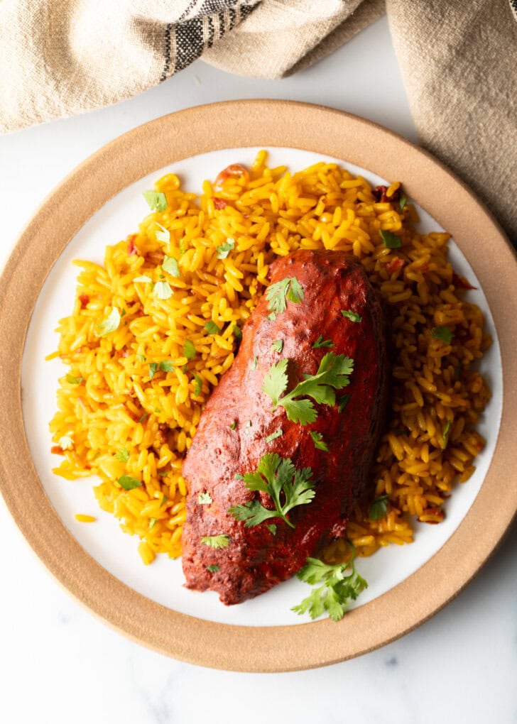 A plate of yellow rice and pollo pibil chicken breast.