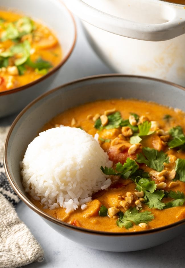 Close view of West African peanut butter soup in a bowl, with scoop of white rice and topped with chopped cilantro and crushed peanuts.