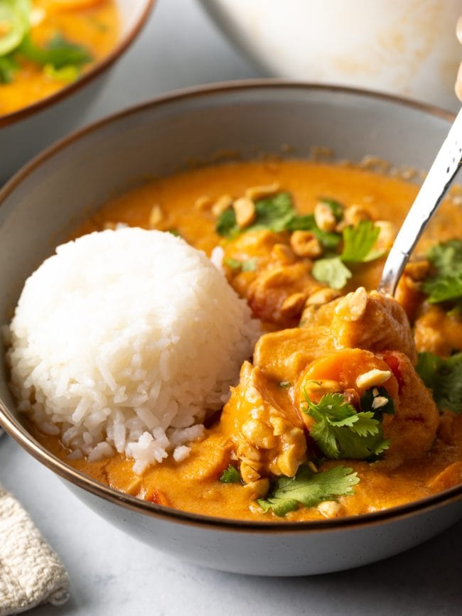 Bowl of Maafe with scoop of rice, metal spoon scooping.