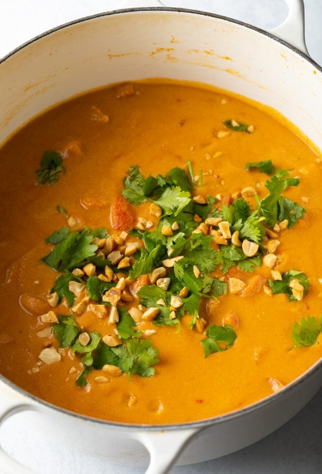 Top view of finished West African peanut soup in cooking pot, topped with chopped cilantro and crushed peanuts.