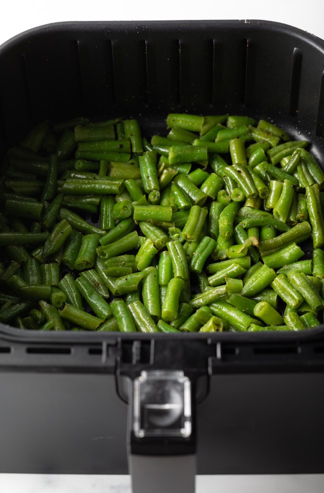 Chopped frozen greenbeans in an air fryer basket.