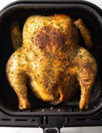 Top down image of whole chicken in an air fryer, cooked with herbs.