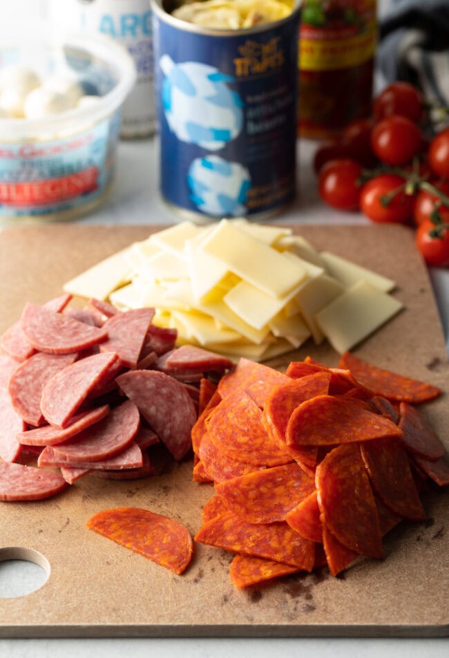 Slices of pepperoni, salami, and cheese on a wooden cutting board.