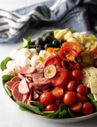 Antipasta salad, loaded with spinach, black olives, mozzarella balls, pepperoni slices, sausage slices, cherry tomatoes, cheese slices, artichoke hearts, and pickled peppers.