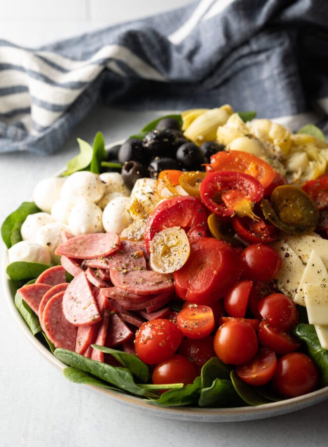 Antipasta salad, loaded with spinach, black olives, mozzarella balls, pepperoni slices, sausage slices, cherry tomatoes, cheese slices, artichoke hearts, and pickled peppers.