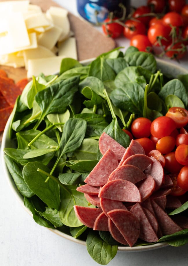 Sliced meats and tomatoes on a bed of spinach.