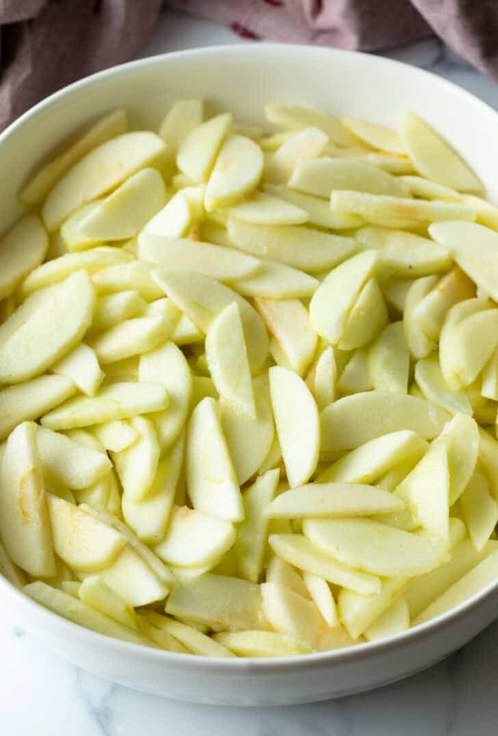 White oval baking dish filled with apple slices.