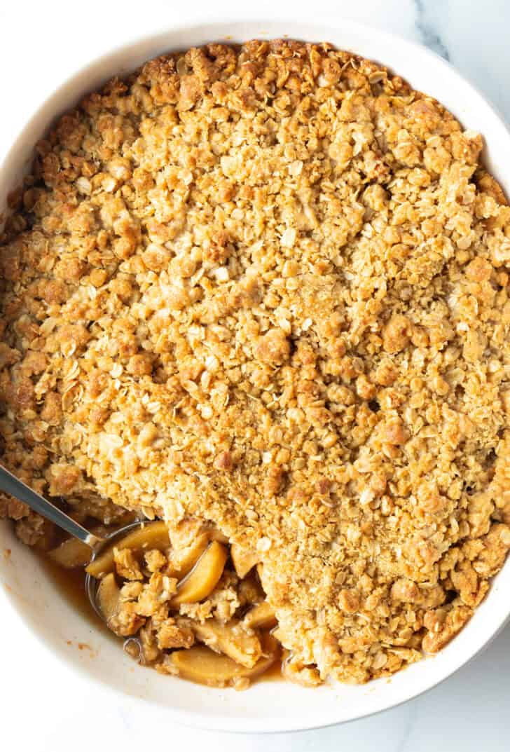 Top down view baked apple crisp with oats. A spoon is scooping away a serving.