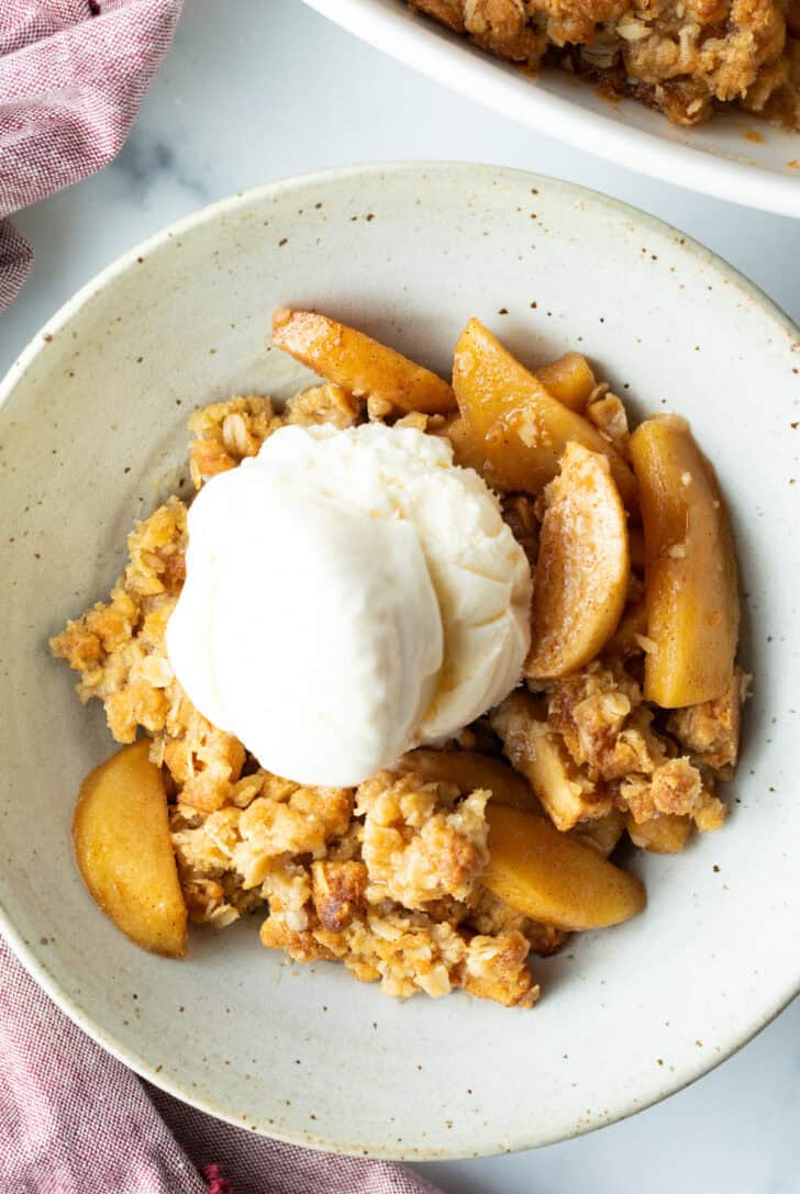 Top down view of a white bowl with golden apple crisp topped with a big scoop of ice cream.