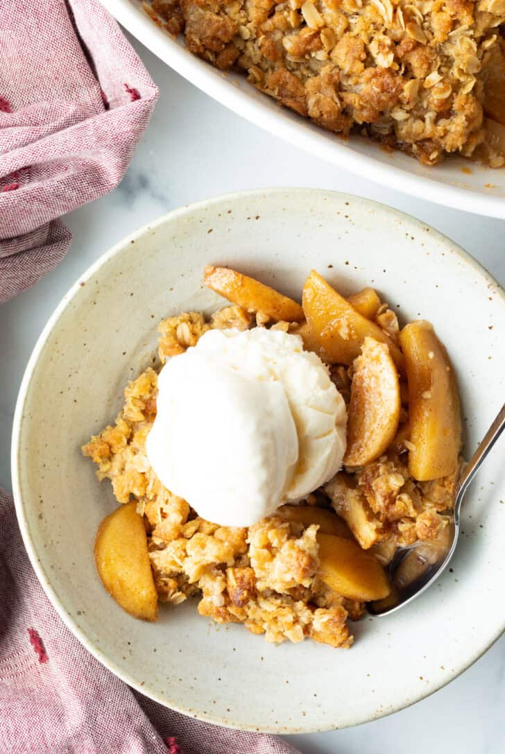 Top down view of a white bowl with golden apple crisp topped with a big scoop of ice cream.