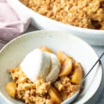 Top down view of a white bowl with golden apple crisp topped with a big scoop of ice cream.