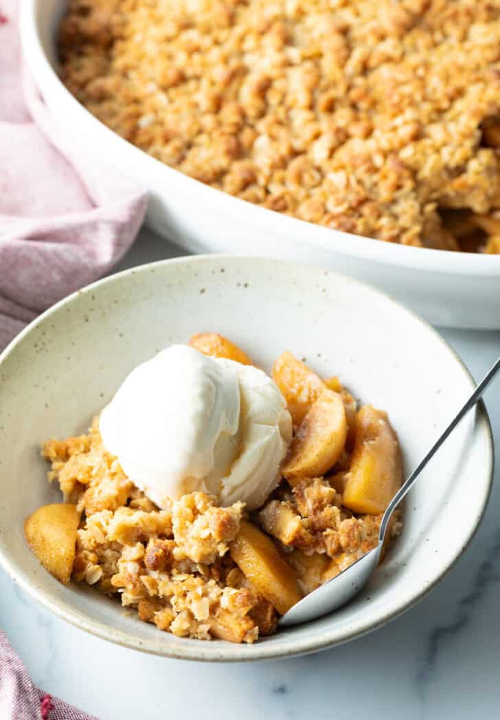 Top down view of a white bowl with golden apple crisp topped with a big scoop of ice cream.