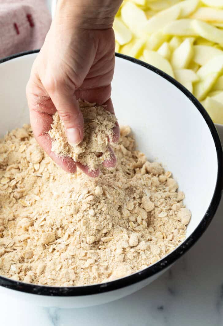 Hand mixing oat crumbly topping in a white bowl.