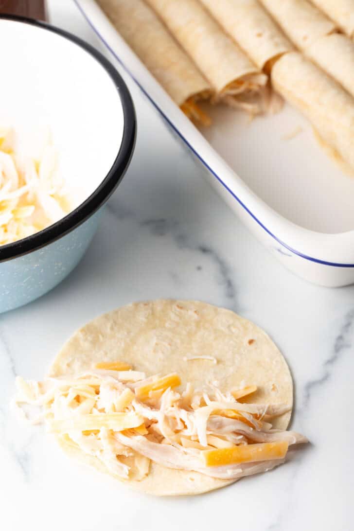 Tortilla with shredded chicken and cheese, ready to roll and place in a baking dish with other enchiladas.