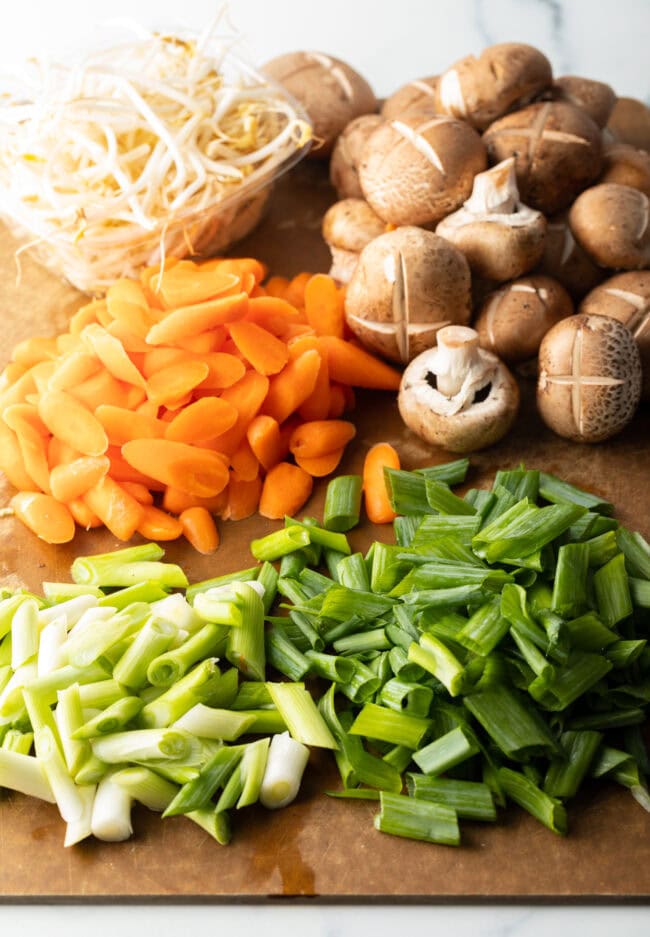 Chopped veggies in piles on a cutting board: mushroom, carrots, and beans.