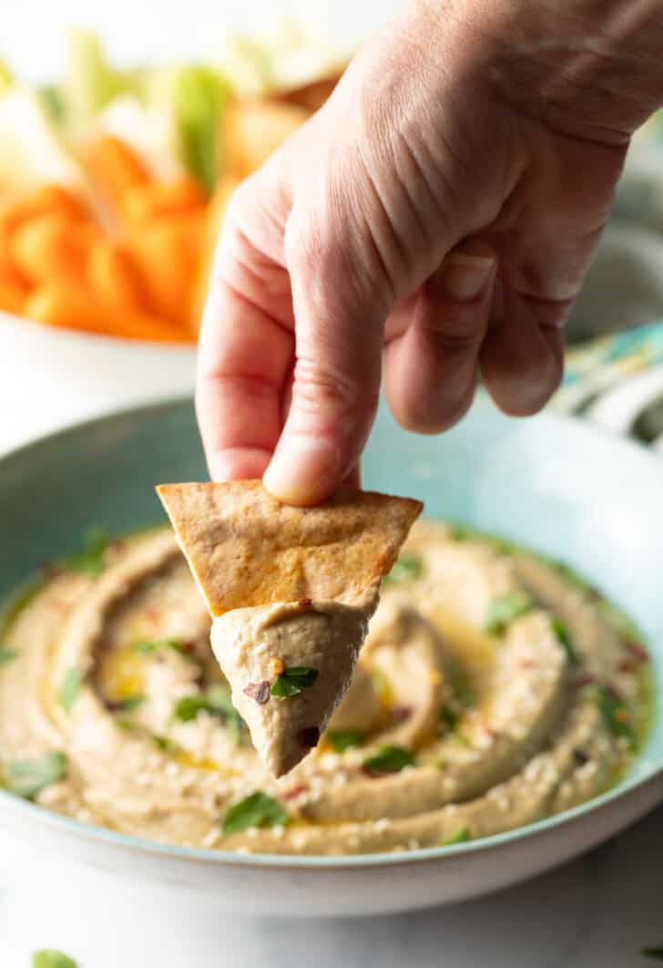 Hand showing a pita chip with eggplant dip to camera.