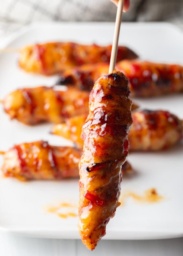 1 bacon wrapped hot sauce coated chicken skewer held up vertically to camera.