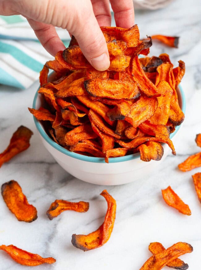 Hand grabbing some carrot chips out of a bowl. 