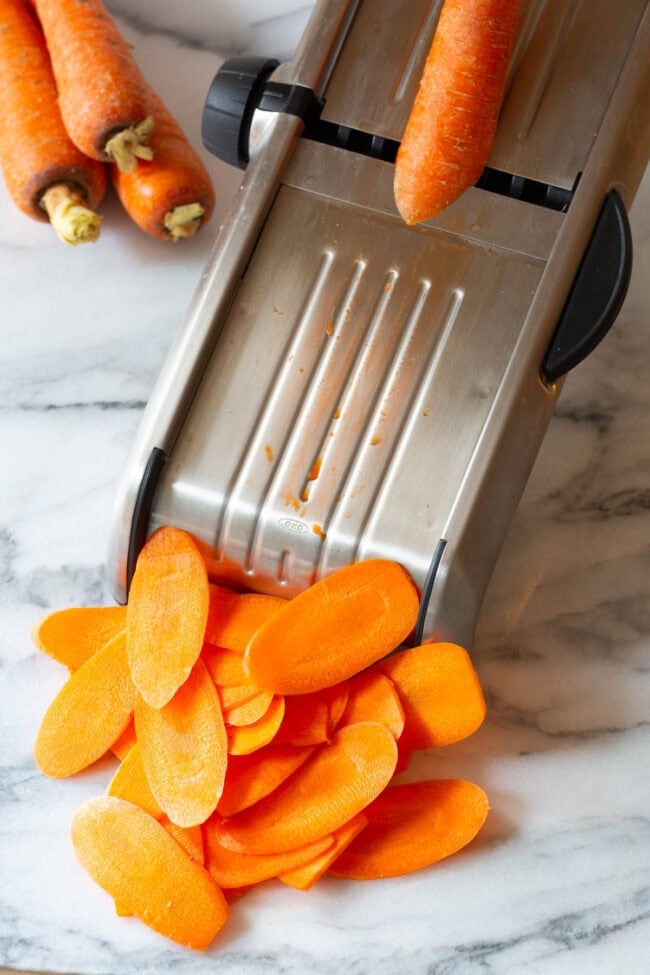 Carrots being sliced on a mandolin slicer. 