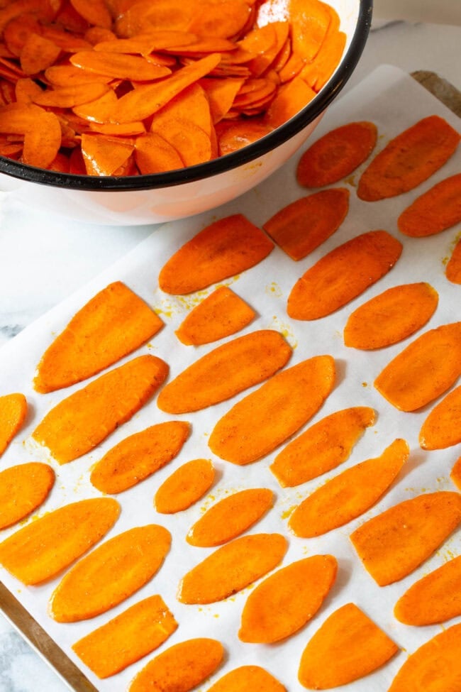 Thinly sliced carrots placed on a baking sheet lined with parchment paper before being baked. 