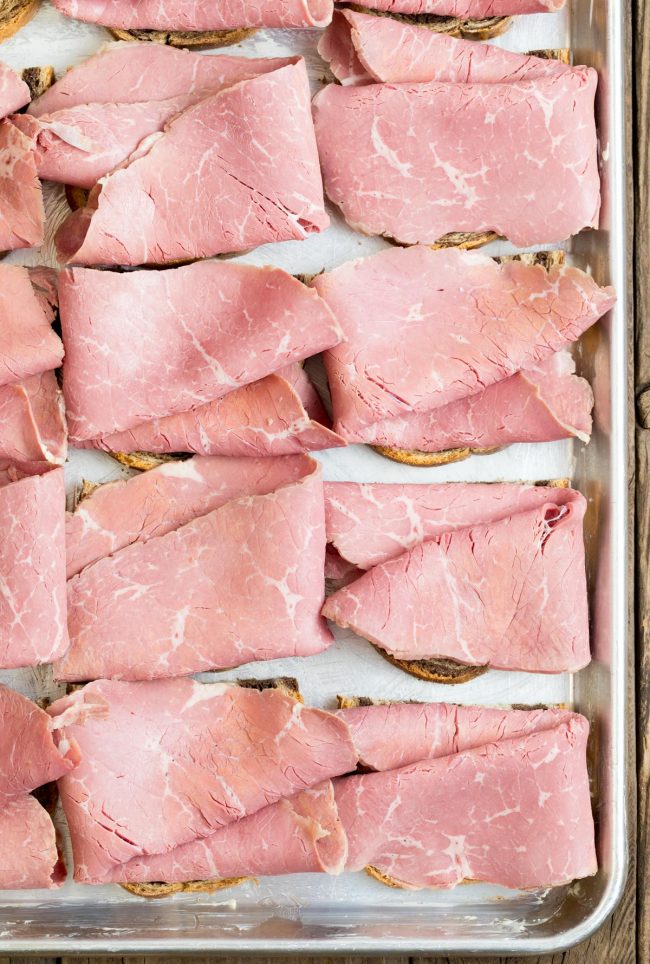 Bread assembled with corned beef slices on a sheet pan. 