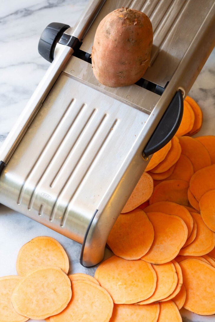 Sweet potatoes being sliced on a mandolin slicer. 