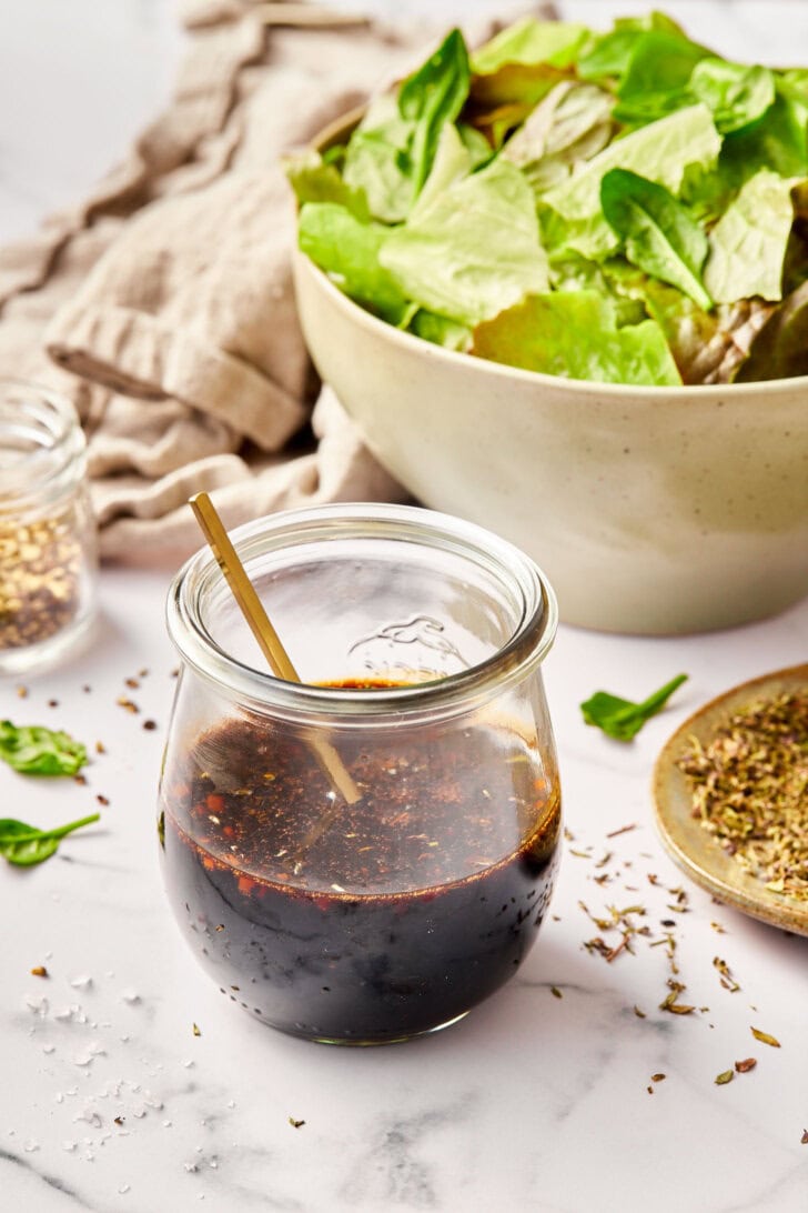 Balsamic vinaigrette in a jar with a salad in the background. 