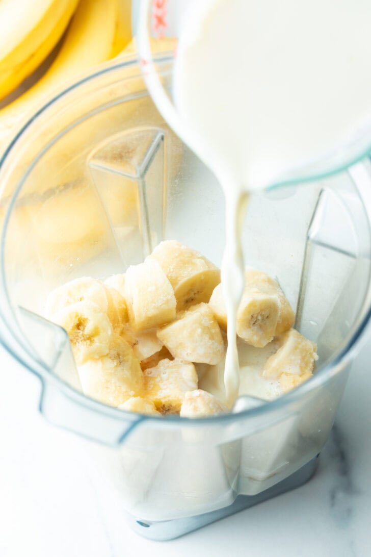 Adding milk to the blender with chopped bananas.