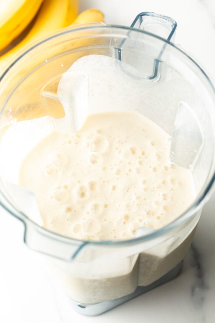 Frothy smoothie with banana in a blender jar.