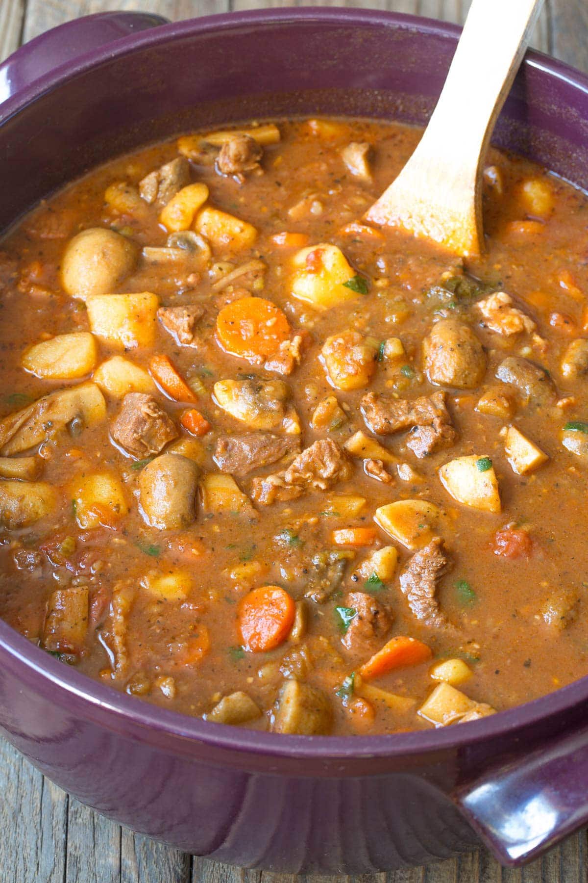 Beef stew recipe in a large pot with a wooden spoon. 