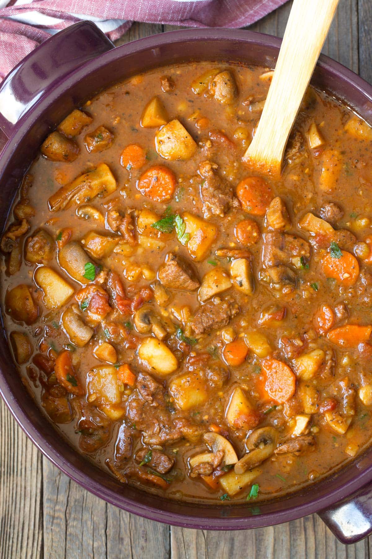 Beef stew in dutch oven with a wooden spoon. 