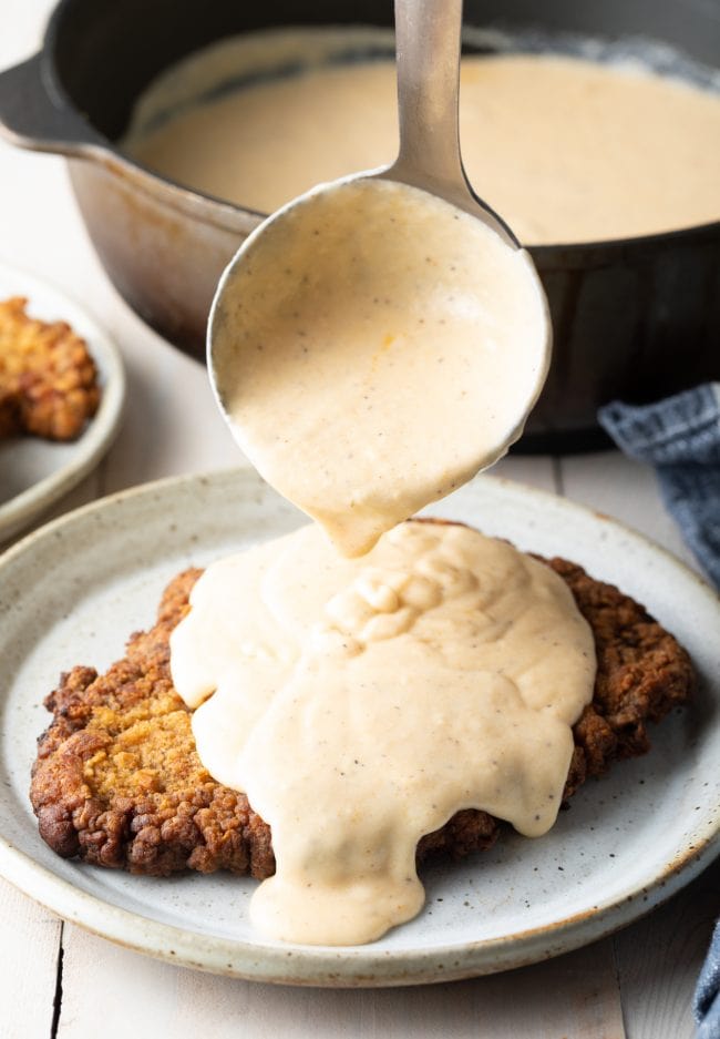 Country fried steak on a plate with a ladle pouring gravy on the top. 