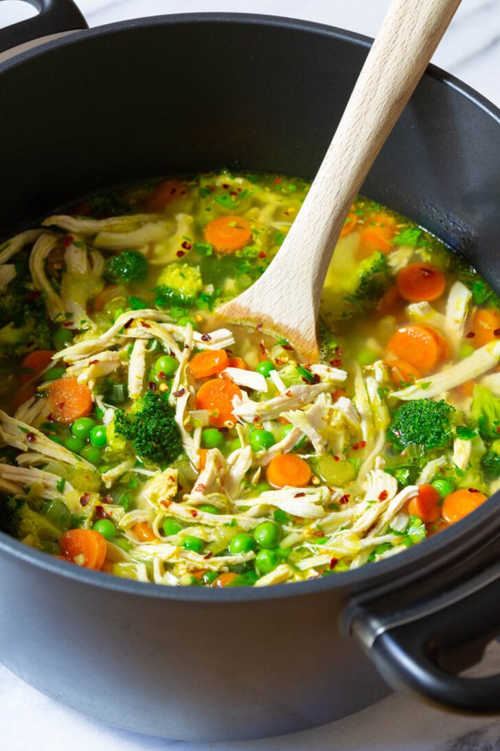 Pot of chicken soup with a wooden spoon stirring it. 