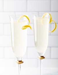 Two drinks in champagne flutes with lemon twist.