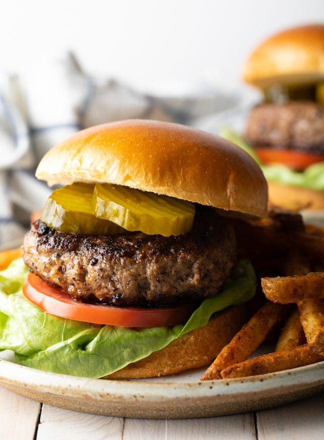 Hamburger with lettuce, tomato, pickles and a bun served with french fries. 